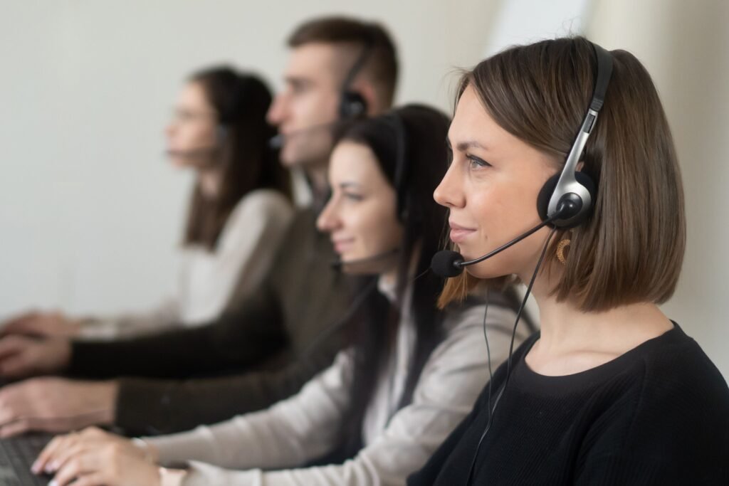 pexels-photo-7035859-7035859 Side view of young coworkers in casual clothes sitting in light workplace with headphones with microphone while surfing on laptop